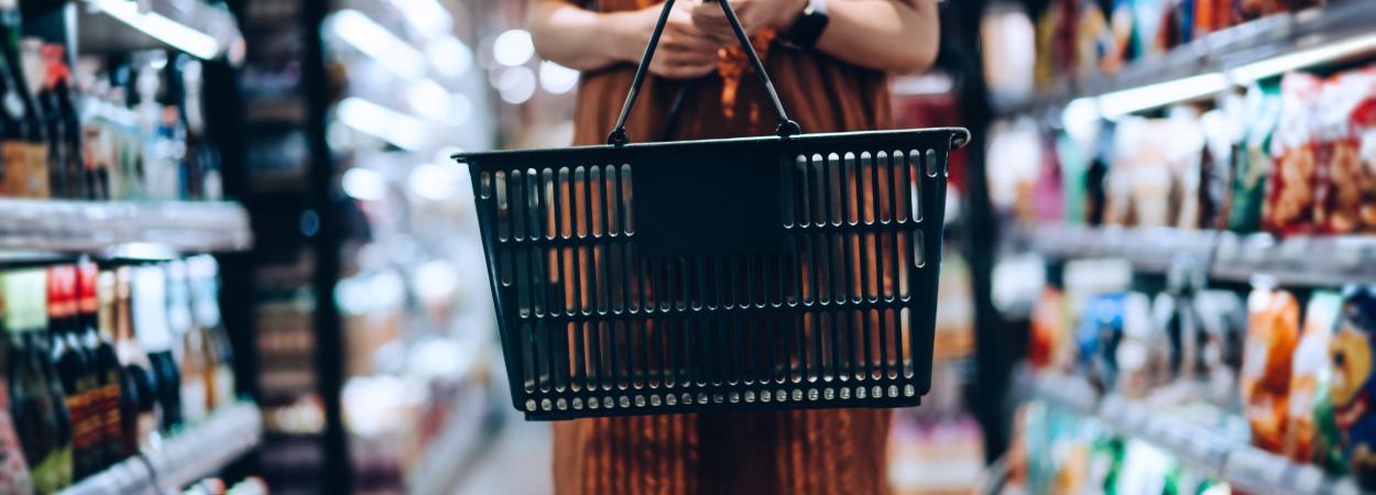 Mulher segura cesto de compras em corredor de supermercado