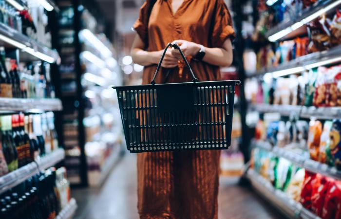 Mulher segura cesto de compras em corredor de supermercado