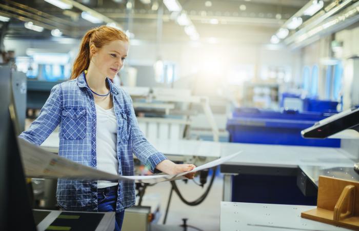 mulher segura páginas junto a máquina de impressão